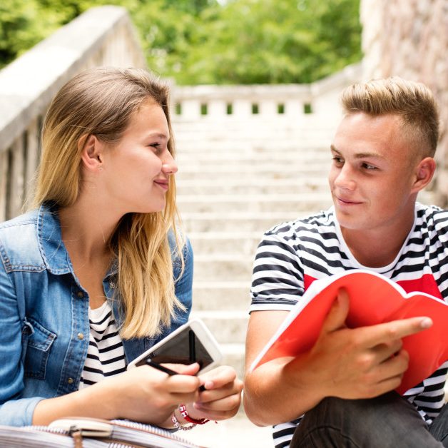 Attractive teenage student couple in front of university studying together.